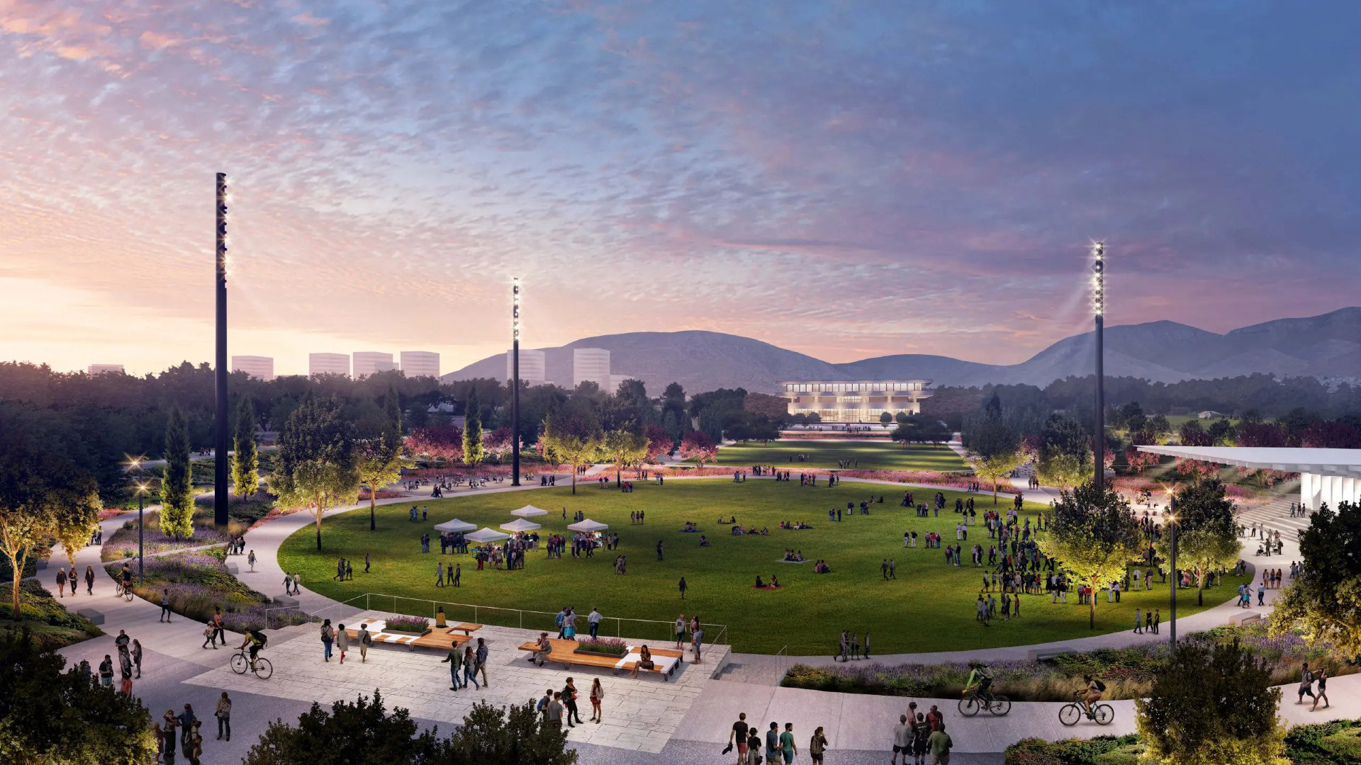 Εικονική βόλτα στο The Ellinikon Park Άνθρωποι σε στρογγυλή πλατεία με γρασίδι, γύρω πεζόδρομοι, δέντρα και κτίρια του The Ellinikon.