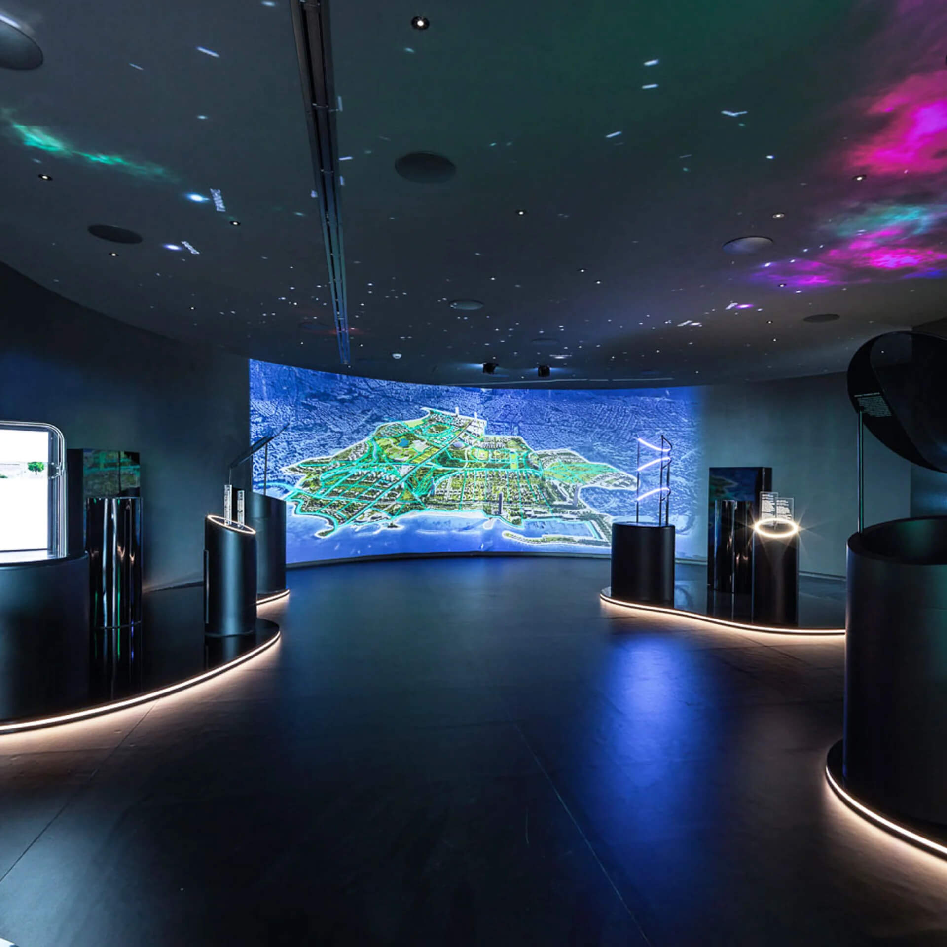 Εσωτερικό του Experience Center Σκοτεινός χώρος με σύγχρονο εξοπλισμό. Στο βάθος το The Ellinikon σε οθόνη και πάνω θόλος με νυχτερινό ουρανό.