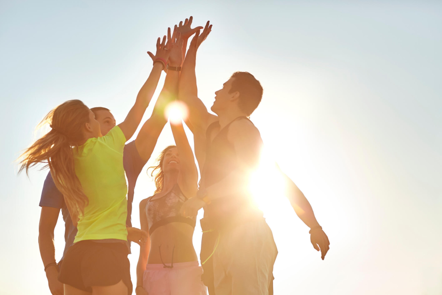After training Two male and two female athletes high-fiving and laughing under the bright blue sky.