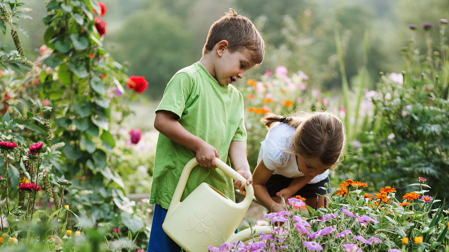 Children at the park A girl and a boy holding a white watering can are tending to colorful flowers in a park.