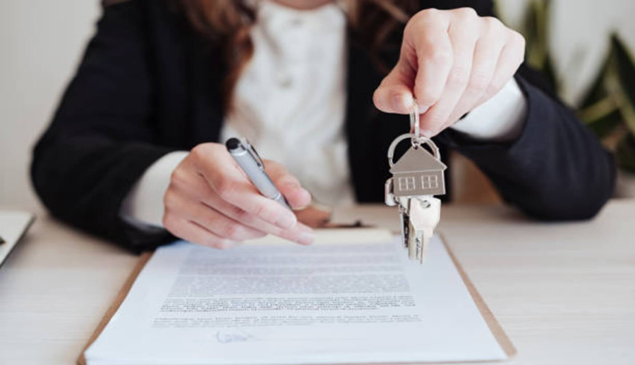 Buying a house Woman in blazer holding a pen and keys on a keychain with a small house. Several documents in front of her.