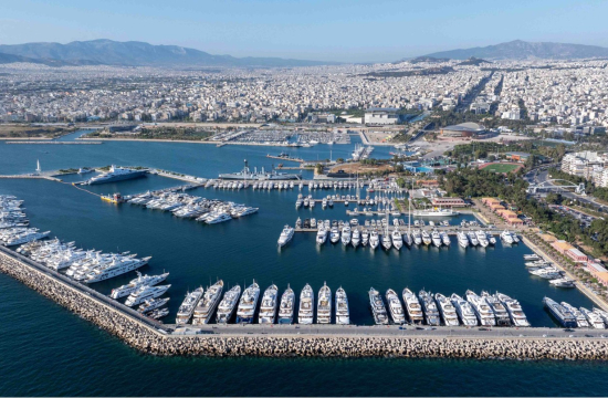 Σειρές σκαφών σε ήρεμη θάλασσα, δεξιά κτίρια και πάρκο κατά μήκος της μαρίνας, πίσω αστικός ιστός. 