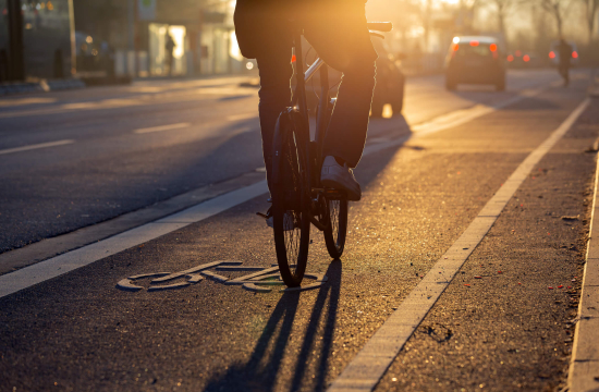 Μπροστά ποδηλάτης, πίσω πεζοί με τσάντες και χαρτοφύλακες, στο βάθος ουρανοξύστες.