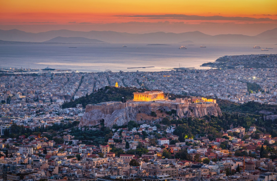 Αθήνα από ψηλά το σούρουπο, στο κέντρο φωτισμένος Παρθενώνας, γύρω κτίρια, πίσω θάλασσα και στο βάθος βουνά.