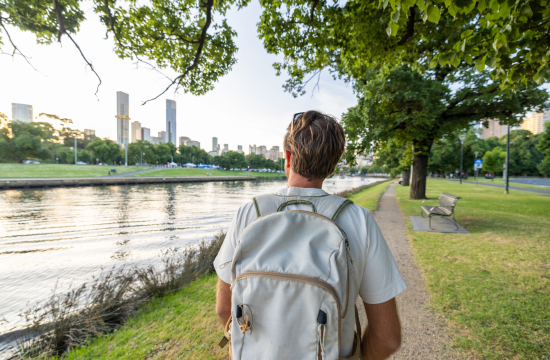 Άντρας περπατά χαλαρά στην πόλη, κοιτάζοντας γύρω του, με το κινητό στην τσάντα. 