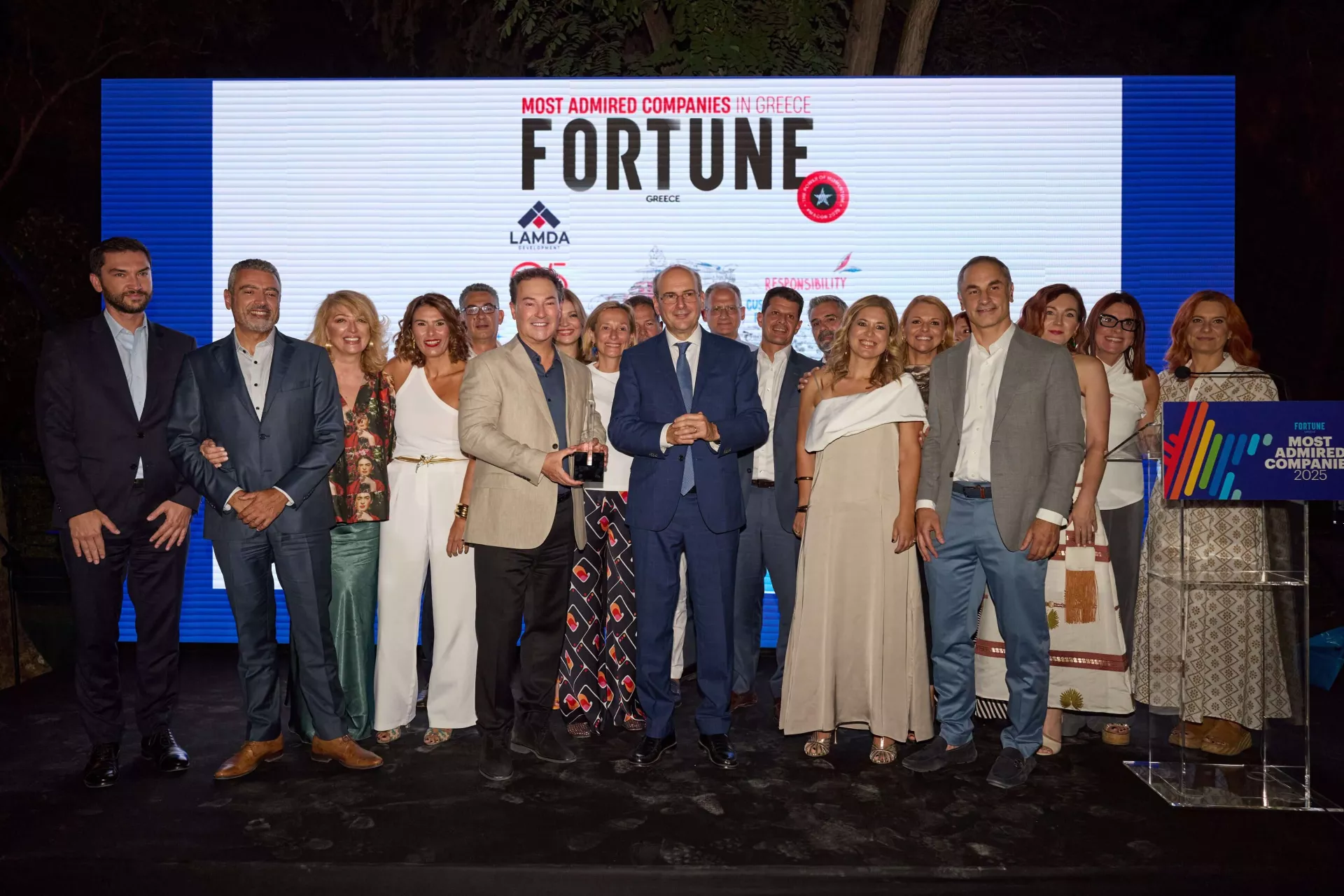 Άνθρωποι μπροστά από λογότυπο Fortune. Στο κέντρο ο CEO Οδυσσέας Αθανασίου με βραβείο, δεξιά ο Κωστής Χατζηδάκης. 
