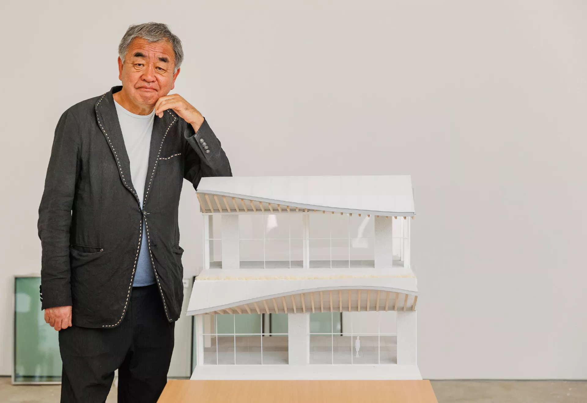 O Κένγκο Κούμα όρθιος και πλάι του μακέτα της Riviera Galleria σε λευκό χρώμα.