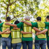 Άνδρες και γυναίκες στη σειρά, με κίτρινα γιλέκα, γυρισμένοι πλάτη, αγκαλιάζονται μπροστά από δέντρα. 
